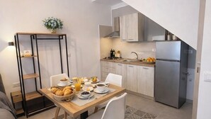 A modern kitchen with a dining area, a small table with breakfast items, and a sofa in the living area. - le casette marconi (Peschici)
