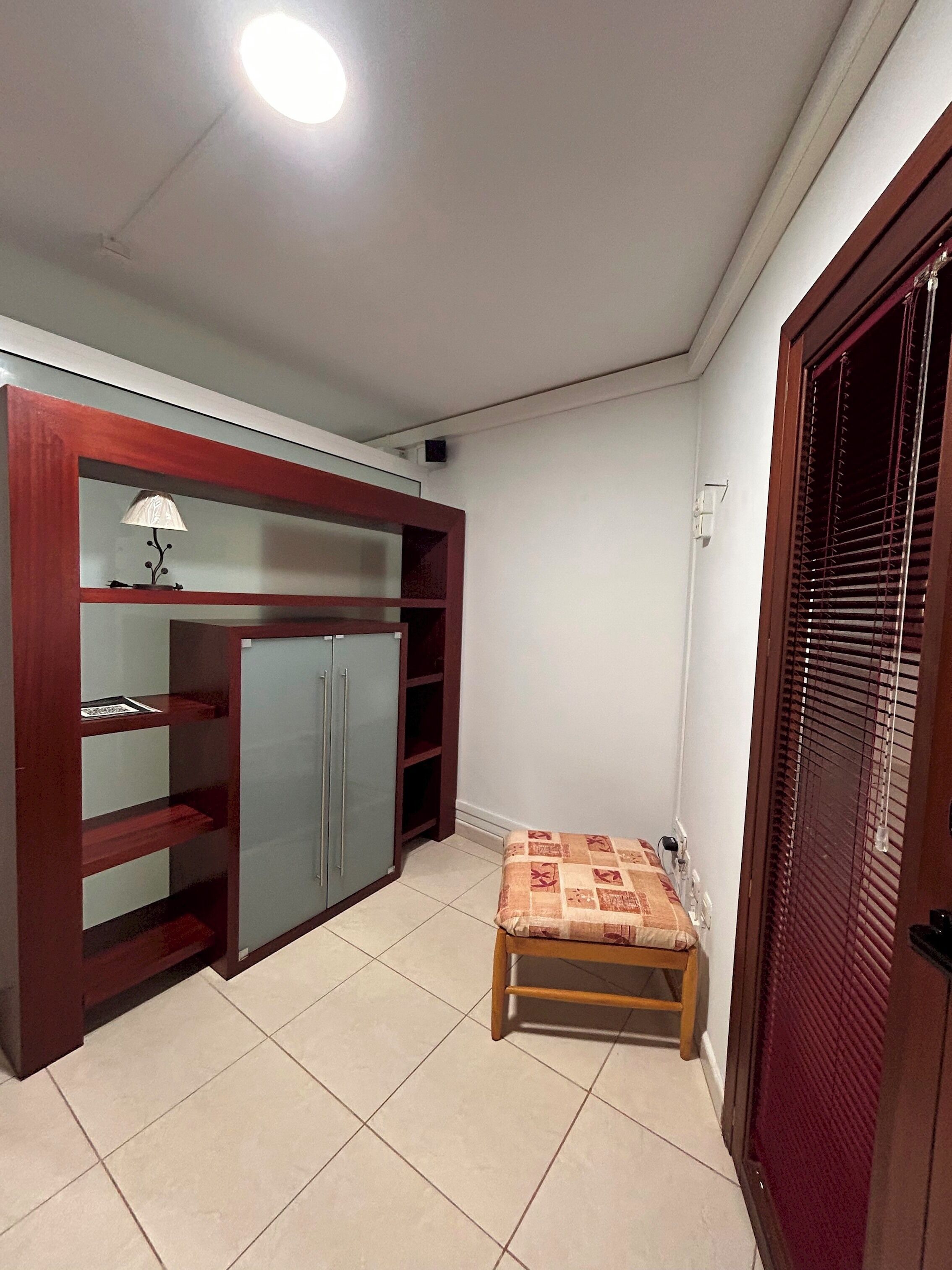 A room with a built-in wardrobe, a small bench, and a door with a window.