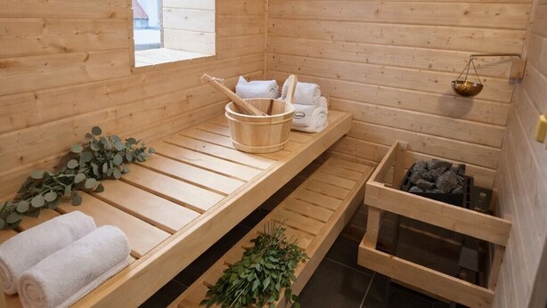 Ein Raum einer Holzsauna mit Bänken, Handtüchern, einem Fenster und einem Steinkopf.