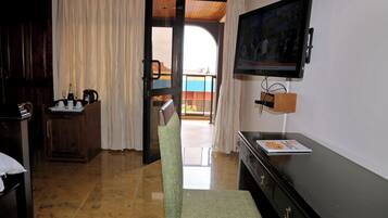 A hotel room with a wooden desk, a chair, a television mounted on the wall, and a view of the outside balcony.