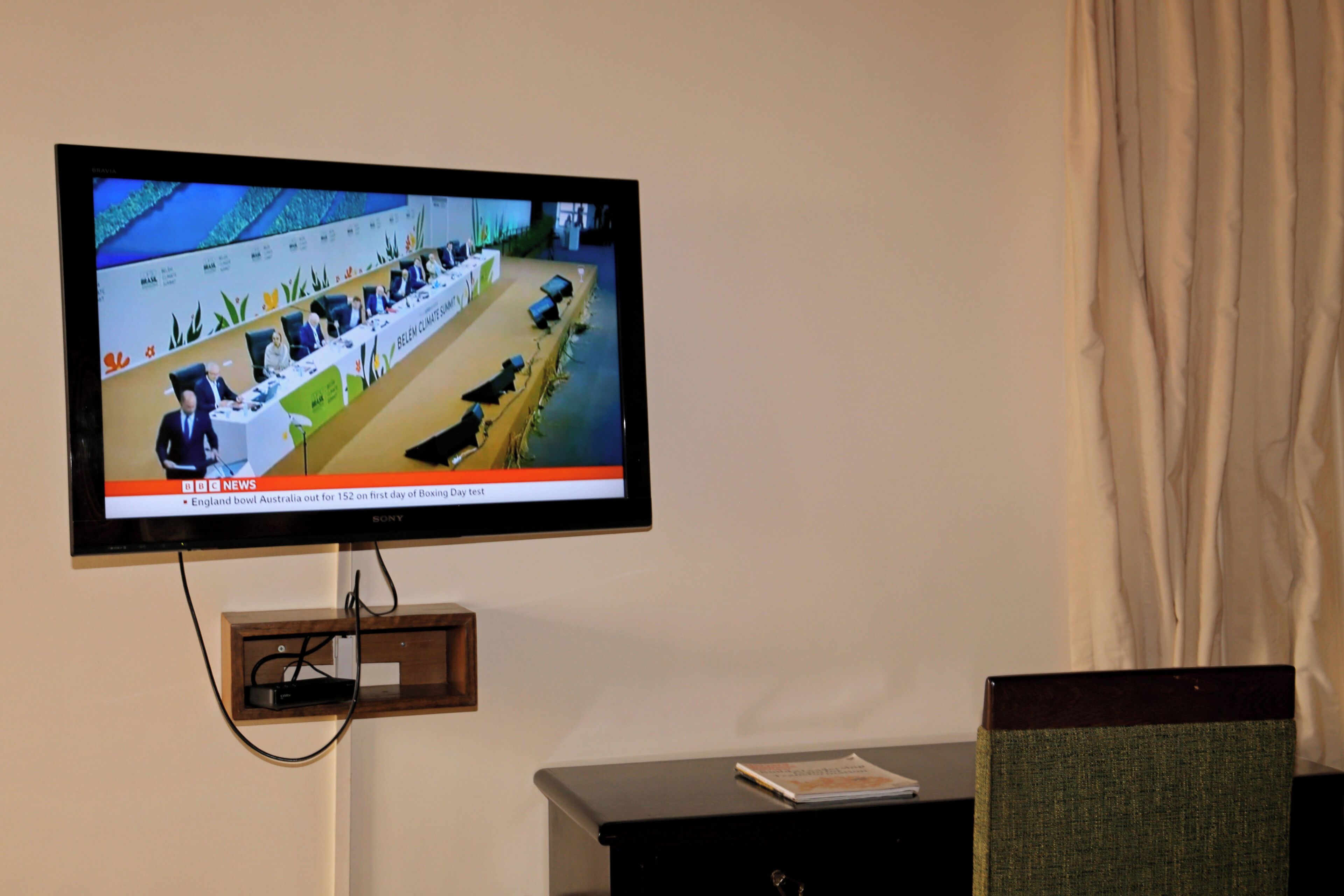 A television mounted on a wall displaying a news broadcast.