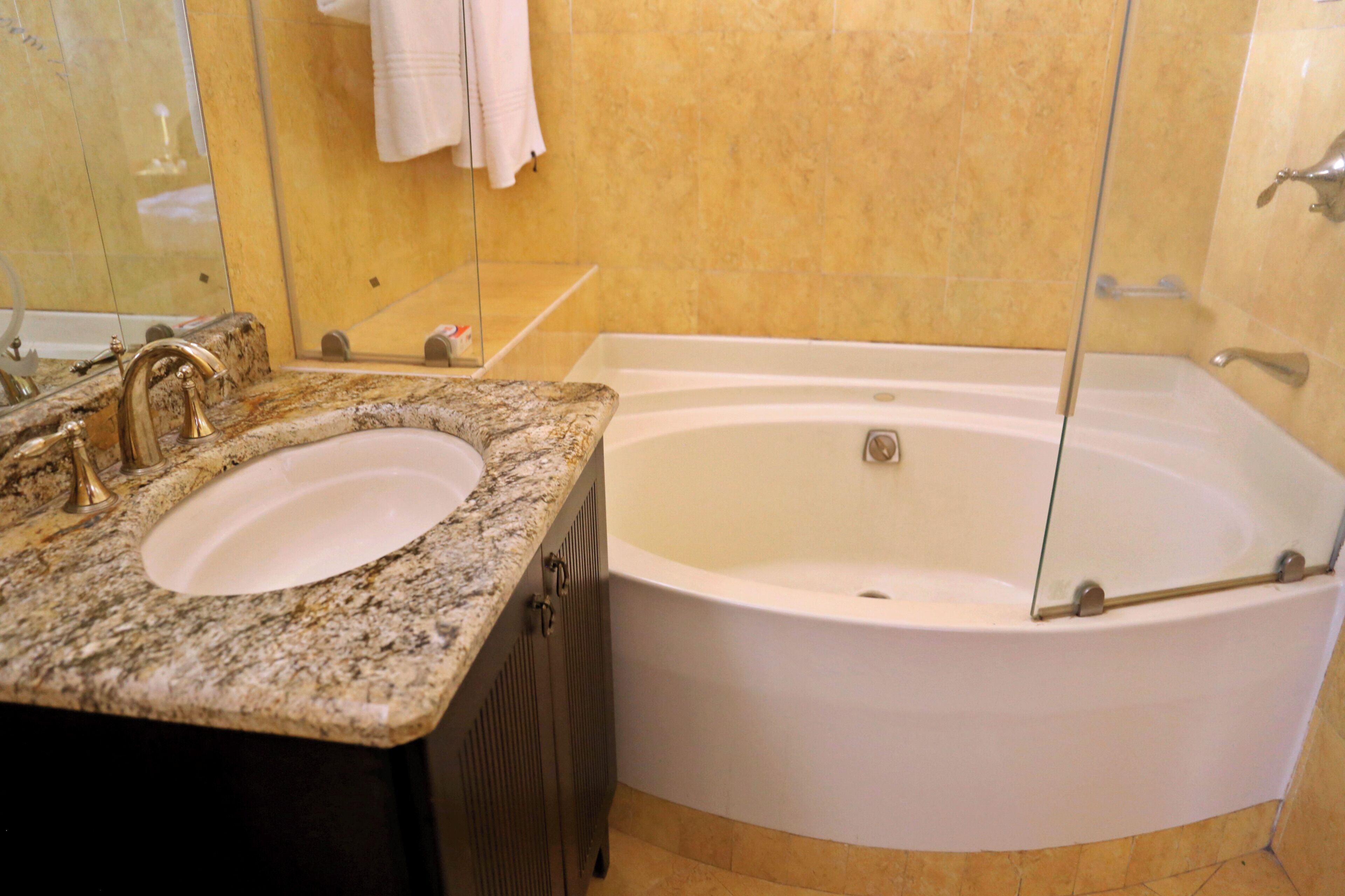 A bathroom with a granite countertop, a white sink, a bathtub, and a mirror.