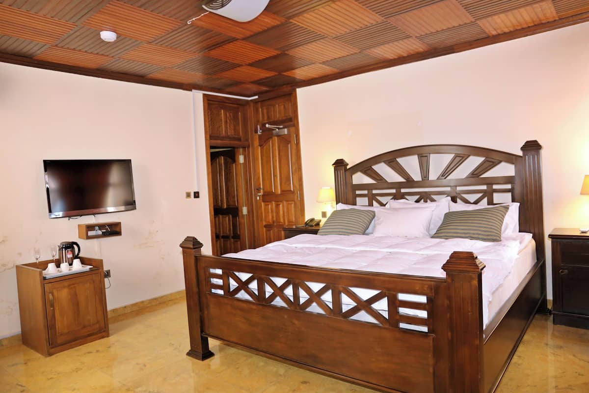 A bedroom with a wooden bed, a television on the wall, a wooden cabinet, and a door leading to another room.