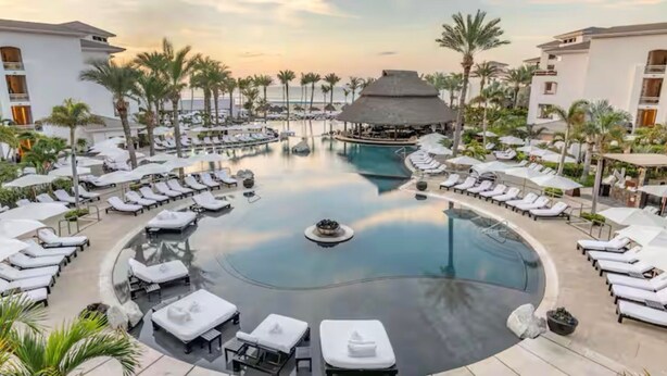 Ein Resort mit einem zentral gelegenen Infinity-Pool, Liegestühlen und Palmen.