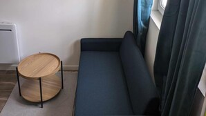 A small room with a dark sofa, a round wooden table, and a window with curtains. - Entire apartment - Angers, France (Angers)