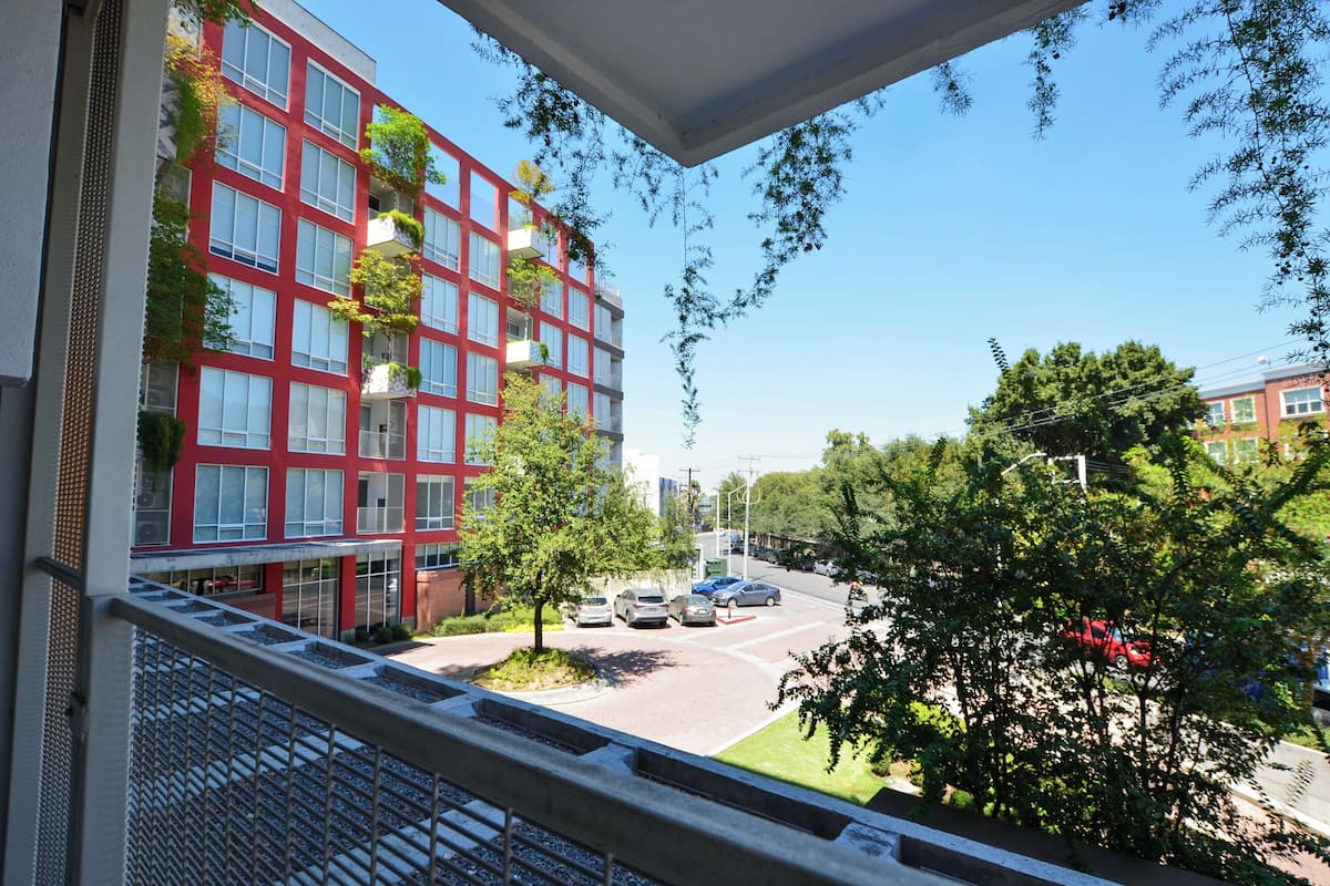 Un edificio rosso con diverse finestre e balconi, una strada con auto parcheggiate e alberi sullo sfondo.