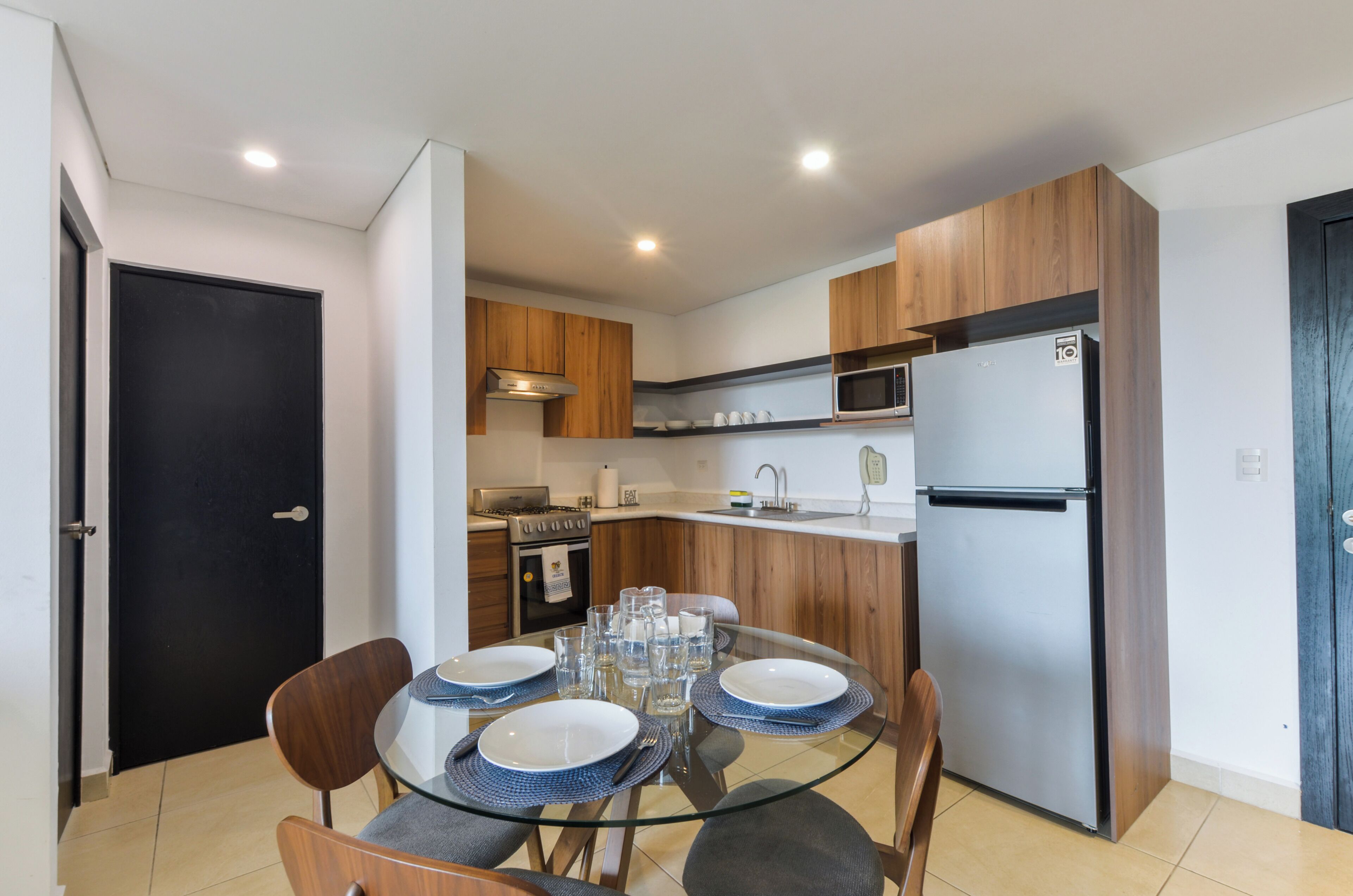 A modern kitchen with a microwave, stove, and refrigerator. There is a dining table with chairs and plates set for four.
