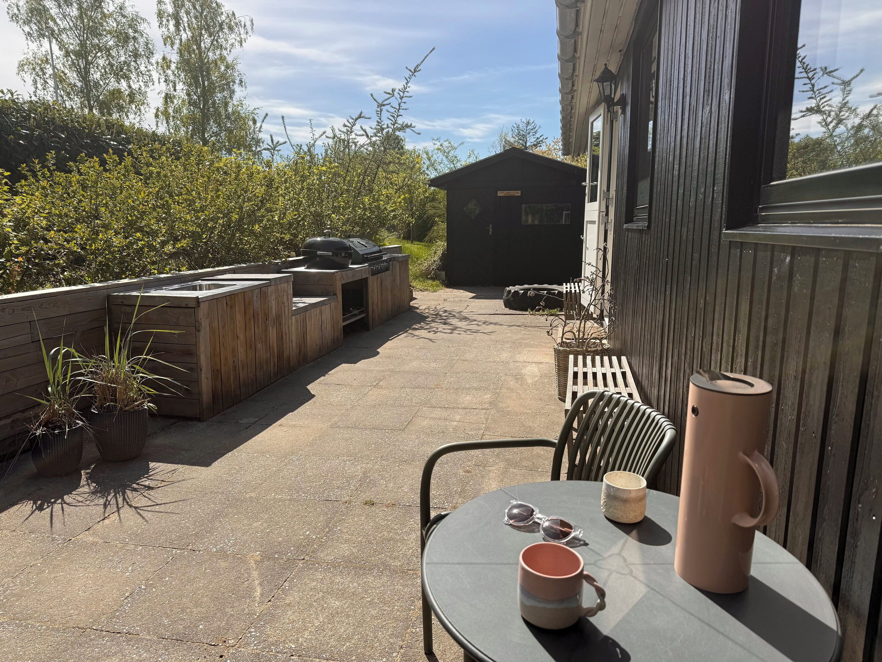 Eine Terrasse im Freien mit Tisch, Stühlen, einem Grill und einem Schuppen.