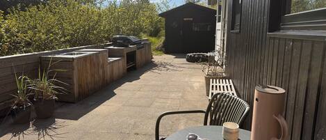 Eine Terrasse im Freien mit Tisch, Stühlen, einem Grill und einem Schuppen.