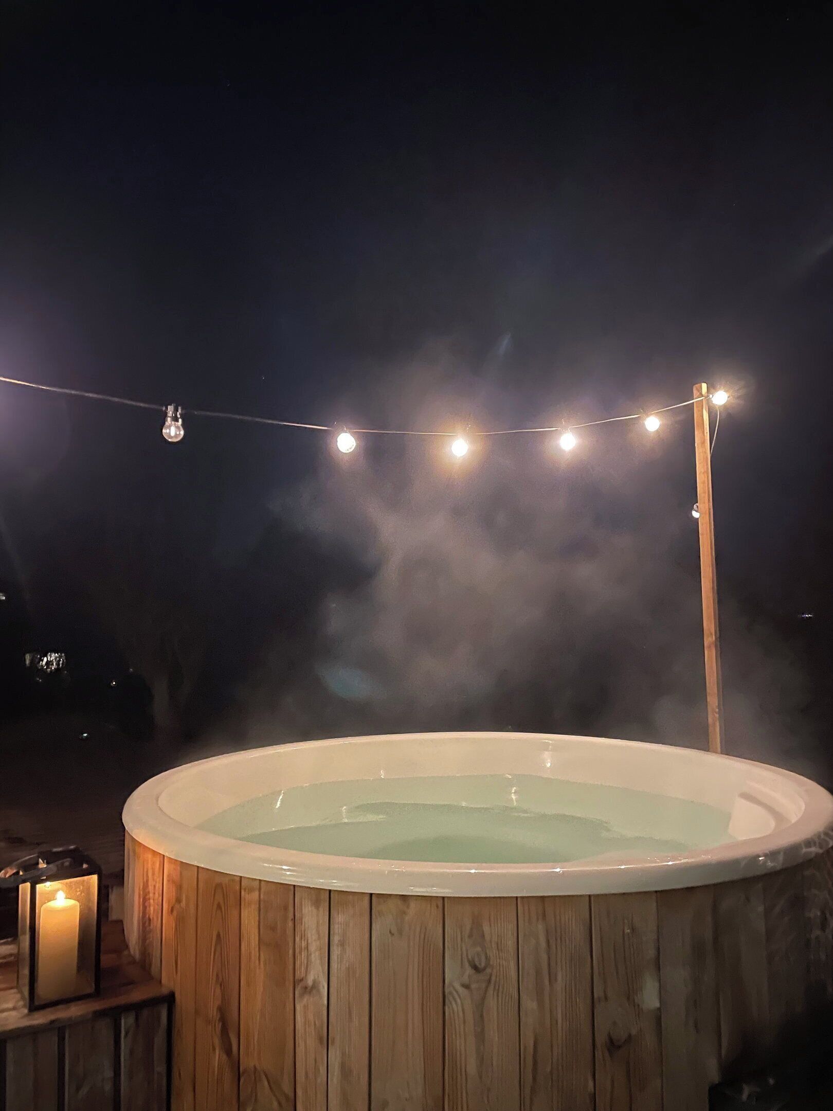 Un bain à remous avec une structure extérieure en bois, entouré d’une guirlande lumineuse.