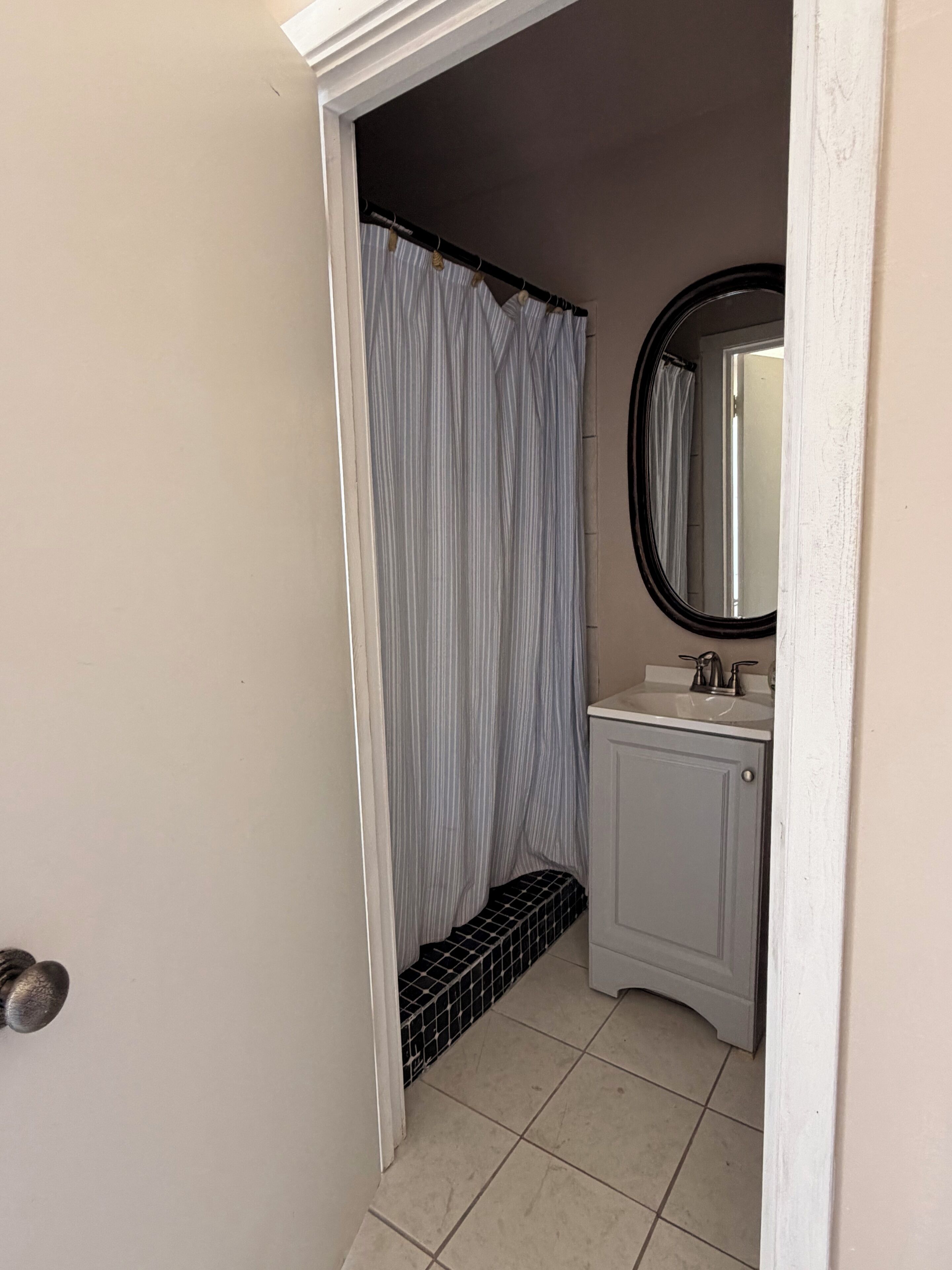 Une salle de bain avec un rideau de douche, un lavabo avec un miroir et un revêtement de sol carrelé.