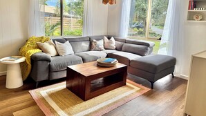 Ein modernes Wohnzimmer mit einer grauen Eckcouch, einem Holztisch und einem großen Fenster mit Vorhängen.