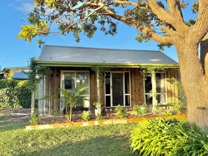 Une maison en bois avec un toit en métal, de grandes fenêtres et un jardin où poussent différentes espèces de plantes.