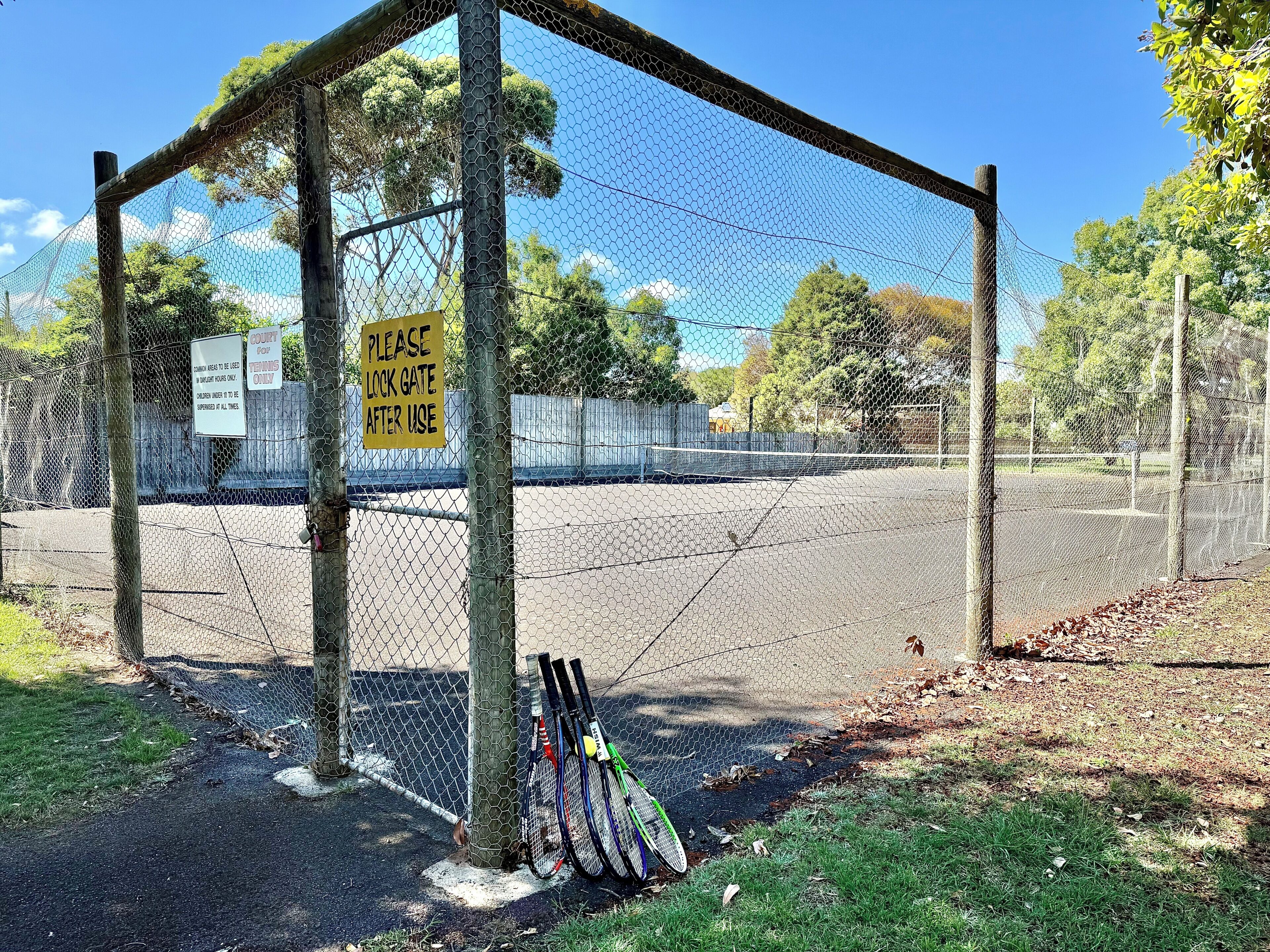 A fenced tennis court with a sign instructing to lock the gate after use.