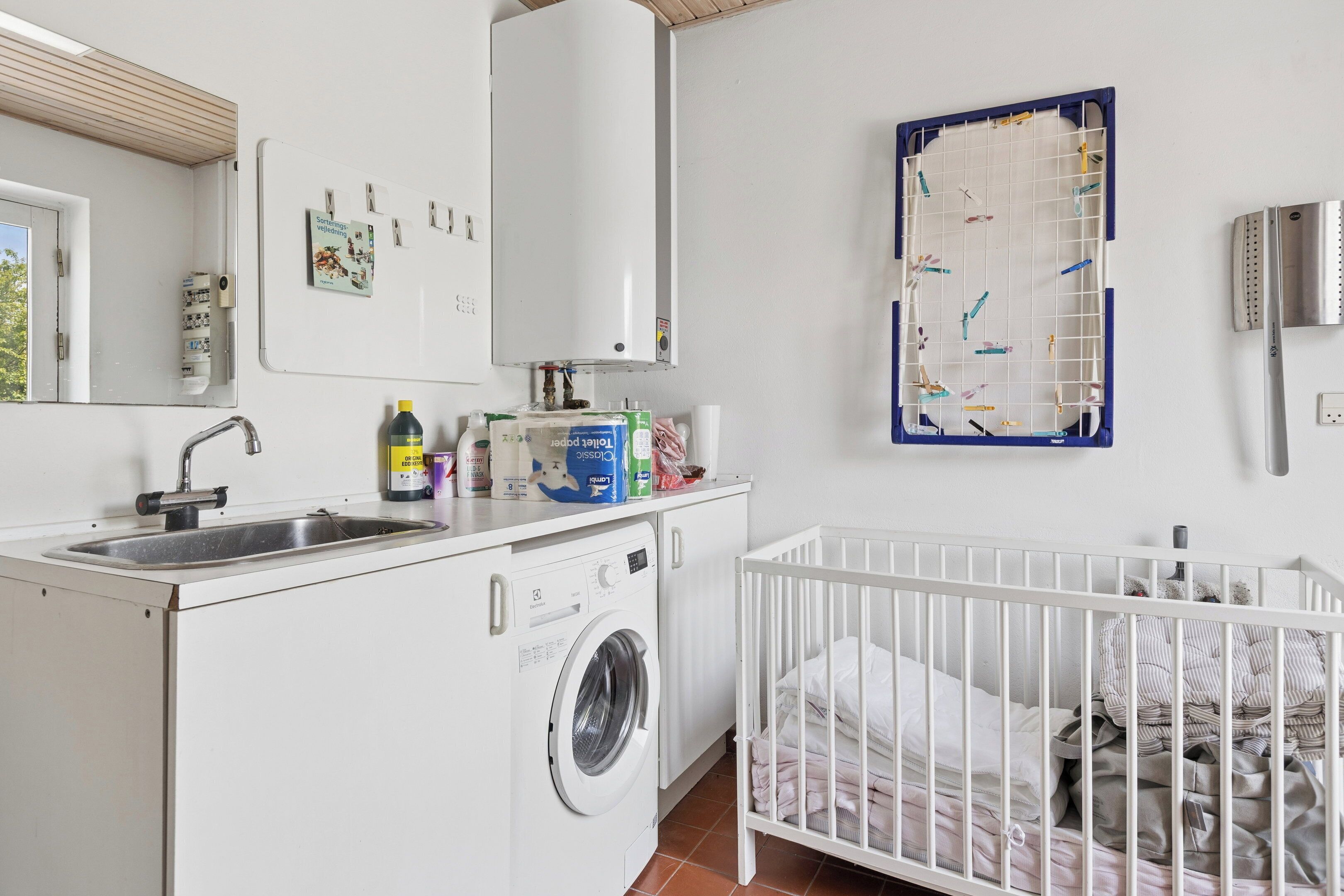 A laundry area with a washing machine, a sink, and a crib.