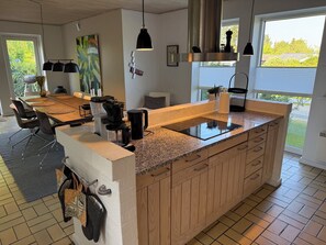 Eine moderne Küche mit einer zentralen Kochinsel, einem Essbereich mit Tisch und Stühlen und Blick auf Grünfläche.