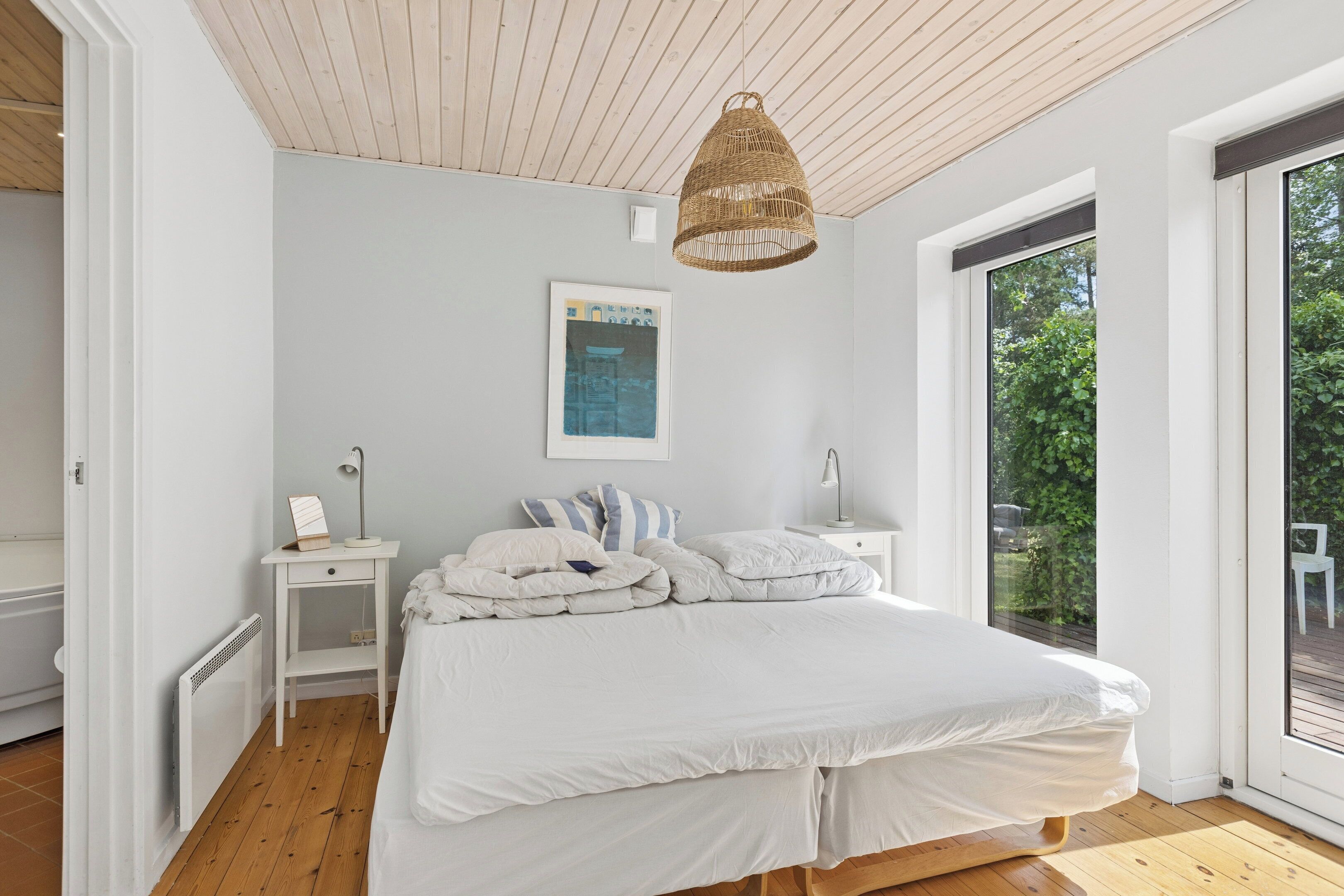 A bedroom with a bed, bedside tables, a hanging light, a window, and a radiator.