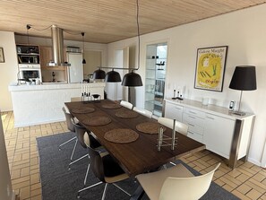 Eine moderne Küche mit einer zentralen Kochinsel, Pendelleuchten und einem Essbereich mit einem langen Tisch und Stühlen.