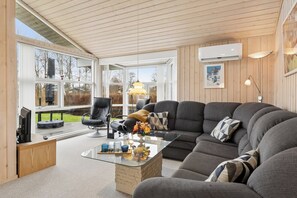 A modern living room with a glass coffee table, grey sofas, and a wooden ceiling.