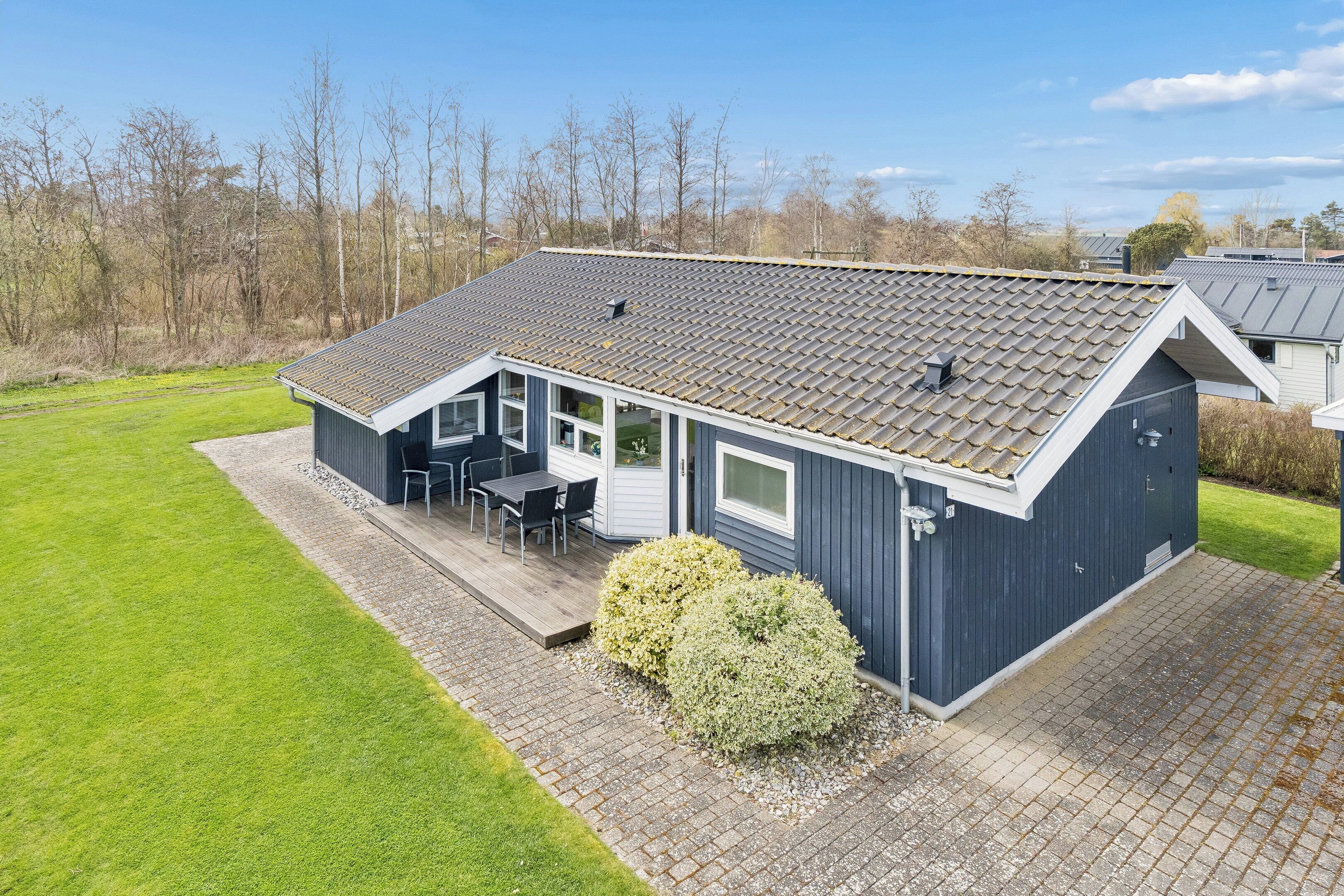 Ein modernes Haus mit Satteldach, einer überdachten Terrasse mit Gartenmöbeln und einem gepflegten Rasen.
