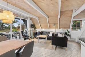 A modern interior with a wooden ceiling, a dining area, a sofa, and a TV. - Charming summer house with a lovely large terrace (Hvide Sande)
