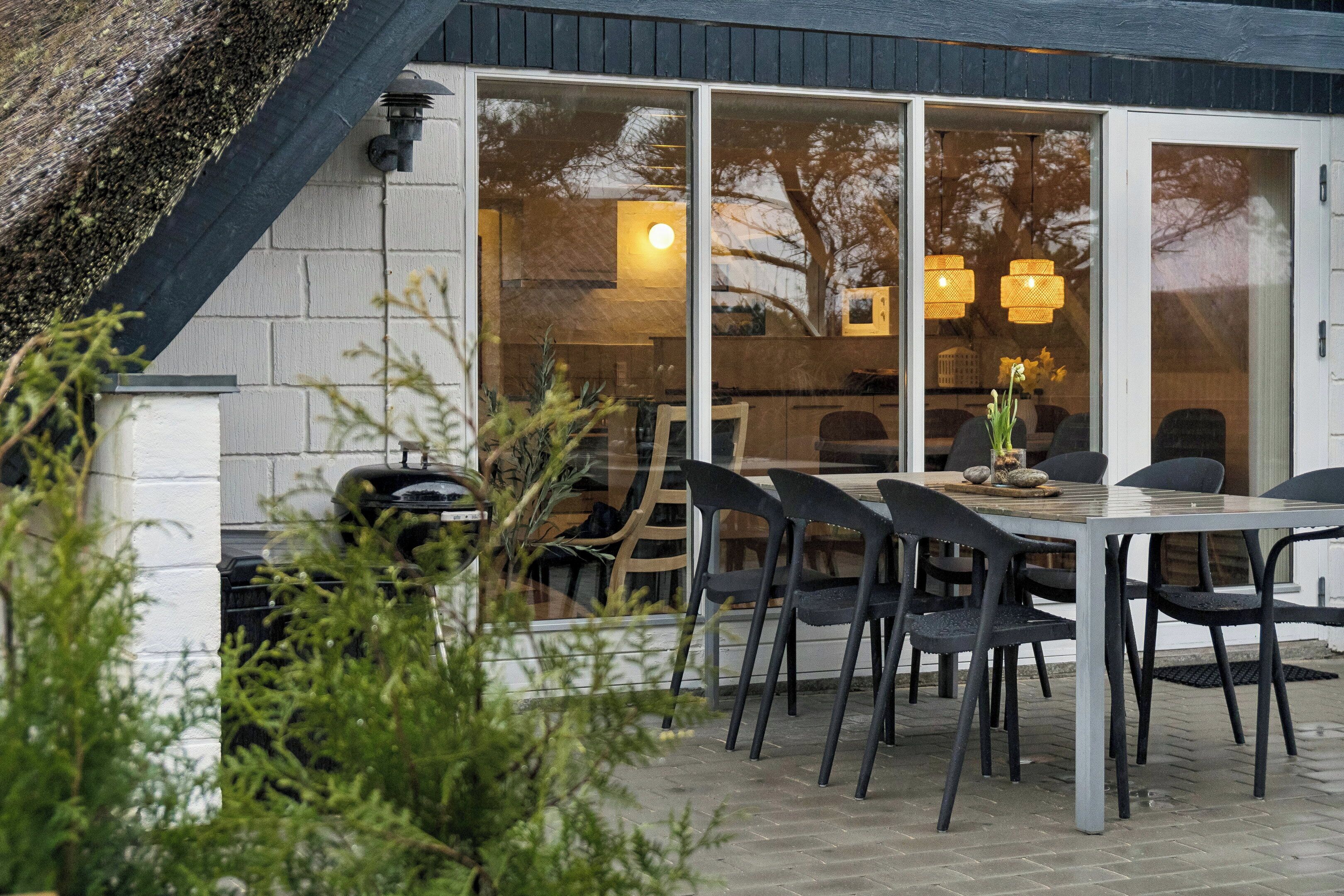 Un coin repas avec une table et des chaises, une fenêtre donnant sur l’intérieur et un mur en briques.