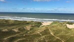 Ett kustlandskap med en strand, gräsklädda sanddyner och havet under en delvis molnig himmel.