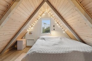 A bedroom with a sloped ceiling, a bed, a window, and string lights. - Charming summer house with a lovely large terrace (Hvide Sande)