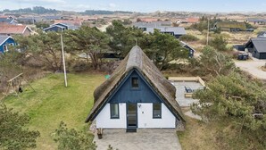 Ett hus med halmtak och blå fasad, omgivet av en gräsyta och träd.