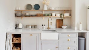 Une cuisine avec un plan de travail blanc, un robinet doré et une étagère en bois au-dessus.