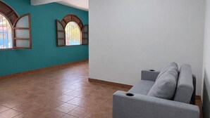 A room with teal walls, a grey sofa, and two arched windows with wooden frames. - Casa Cruz (Brisas de Zicatela)