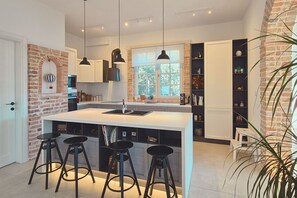Une cuisine moderne dotée d’un îlot central, de tabourets de bar, de luminaires suspendus et d’un mur d’accent en briques.