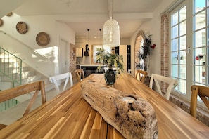 Un comedor con una mesa de madera, sillas, una lámpara colgante y vistas a la cocina.