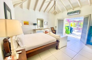 A bedroom with a bed, bedside table, lamp, and a view of the garden through the door.