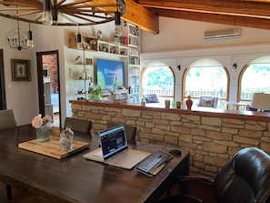 Eine Steinscheibe mit einem Laptop und einer Vase auf einem Holztisch, ein Bücherregal mit Büchern und Dekorationen sowie Blick durch rundbogige Fenster.
