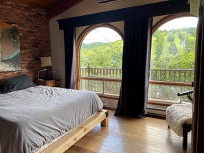 Ein Schlafzimmer mit einem großen Bett, einer hölzernen Bank und Blick auf einen Balkon mit Geländer.