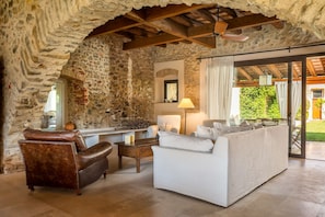 Ein Zimmer mit steinernen Wänden, einer Couch, einem Ledersessel, einem Tisch und einer Lampe.