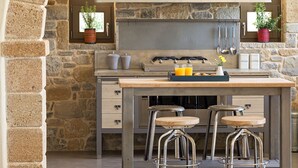 A kitchen with a stone wall, a wooden island with stools, a gas stove, and potted plants. - Villa Marat - Four Bedroom Villa, Sleeps 8 (Astratigos)