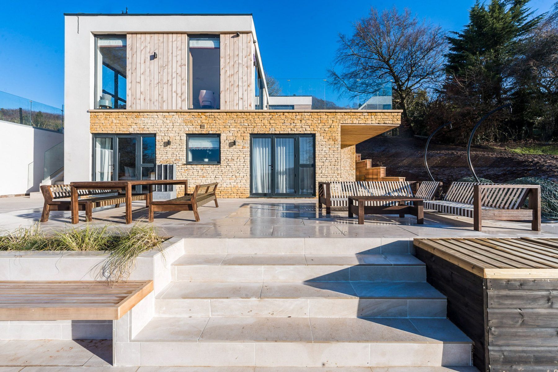 Een modern huis met een stenen gevel, grote ramen en een terras met tuinmeubilair.