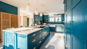 A modern kitchen with teal cabinetry, a central island, pendant lighting, and a window with a view. - Elysian Heights - Five Bedroom Villa, Sleeps 10 (Cheltenham)