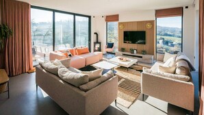 A modern living room with a fireplace, large windows, and a flat-screen TV. - Elysian Heights - Five Bedroom Villa, Sleeps 10 (Cheltenham)