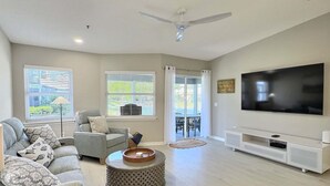 A spacious living room with a grey sofa, a white armchair, a TV, and a ceiling fan. - ALL NEW - Resort Amenities and Beach Access (Siesta Key)