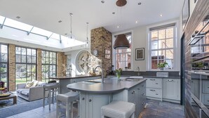 A modern kitchen with a large island, bar stools, and a stone fireplace. - Greenwich Hall - Nine Bedroom Villa, Sleeps 22 (London)