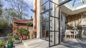 A modern house with a glass door leading to a patio area with outdoor furniture. - Greenwich Hall - Nine Bedroom Villa, Sleeps 22 (London)