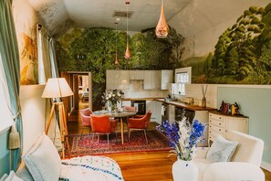 Una sala de estar acogedora con comedor, una cocina con armarios blancos y un mural verde en la pared.