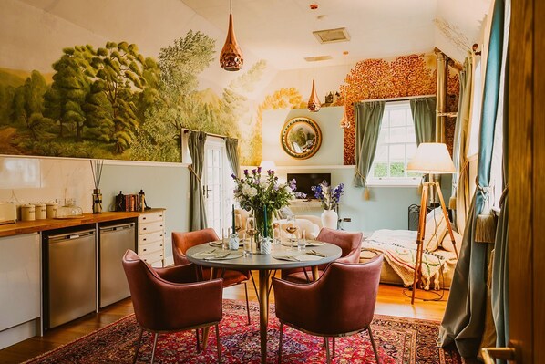 A dining area with a round table, two chairs, a vase with flowers, and a television in the background.