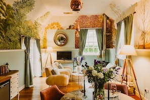 A cozy living room with a television, comfortable seating, a fireplace, and a decorative wall mural.
