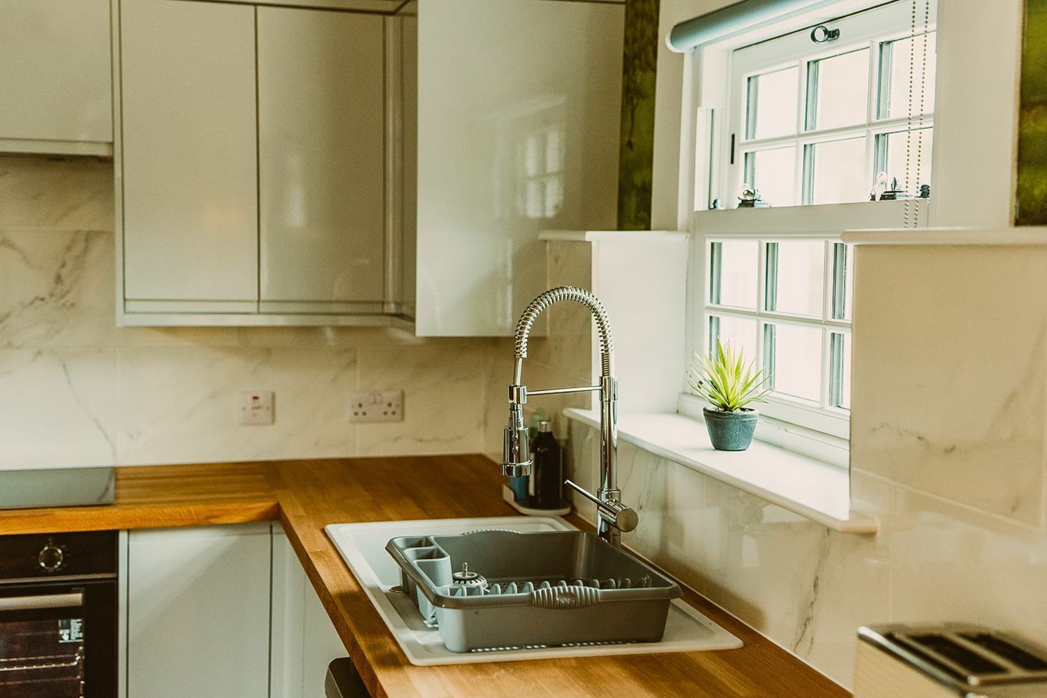 A kitchen with a built-in dishwasher, a sink with a flexible faucet, and a window with a potted plant.