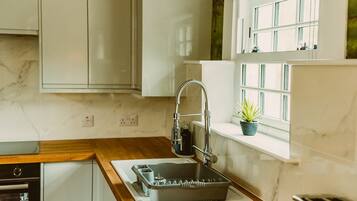 A kitchen with a built-in dishwasher, a sink with a flexible faucet, and a window with a potted plant.