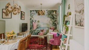 Um quarto com um mural, uma área de jantar, uma cadeira rosa e uma estante de livros.